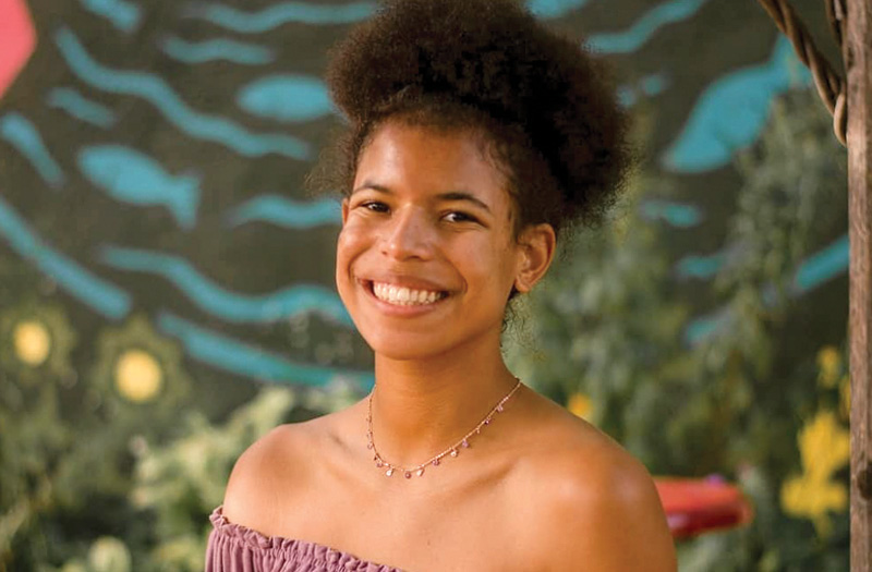 A smiling woman wearing a summer dress and a necklace.